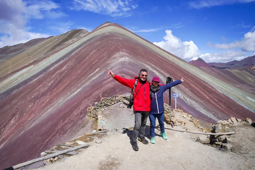 Capture your adventure on Rainbow Mountain: Panoramic views of the Andes Two hikers posing at the summit of Vinicunca Rainbow Mountain in Cusco, Peru