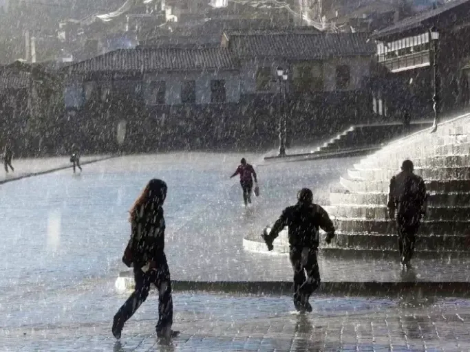 People walking across the wet Plaza de Armas in Cusco during a rainy day in the Andes