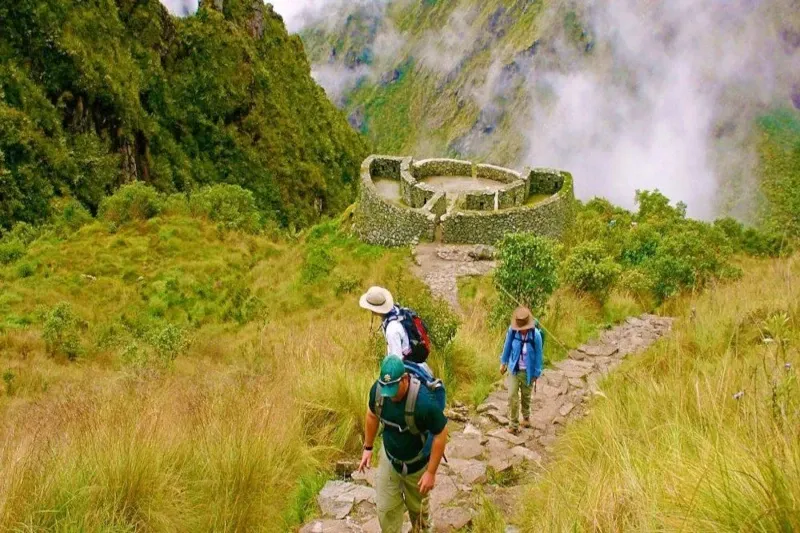 Aerial view of the circular Runkurakay ruins surrounded by lush green mountains and misty clouds.