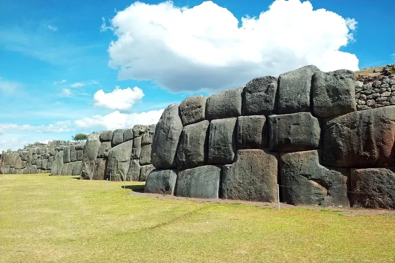 Massive carved stone walls of the Sacsayhuaman archaeological site under a blue sky in Cusco, Peru.