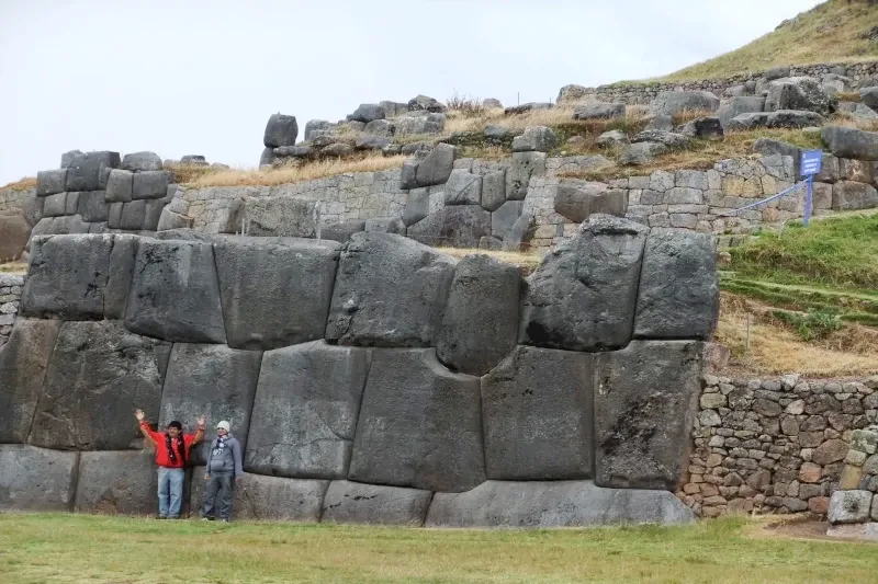 Two travelers standing next to the massive, precision-cut stone walls of the Sacsayhuaman Incan fortress in the hills above Cusco.