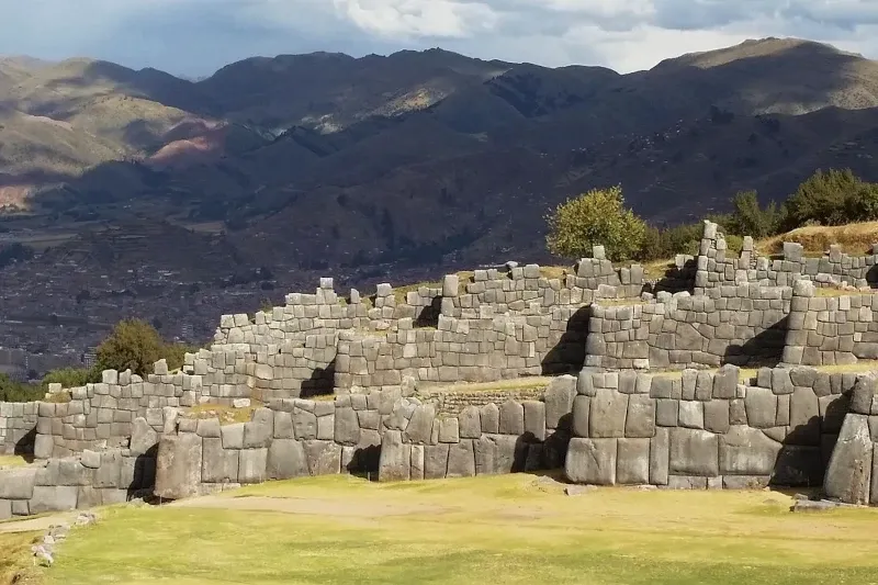 Impressive zigzag megalithic stone walls of Sacsayhuamán archaeological park with mountains in the background.