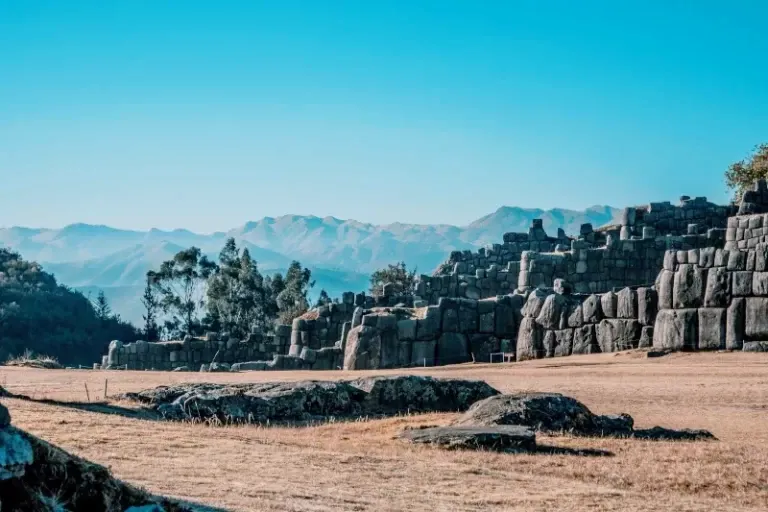 Panoramic view of the ancient Inca ruins of Sacsayhuaman with the Andes mountains in the background under a clear blue sky.