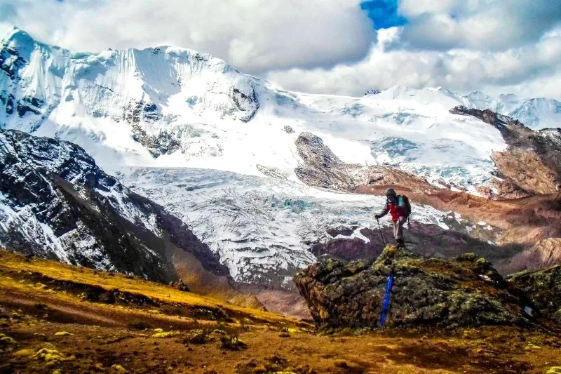 A hiker standing on a rock overlooking the massive Humantay and Salkantay snow-capped mountain range in Cusco, Peru.