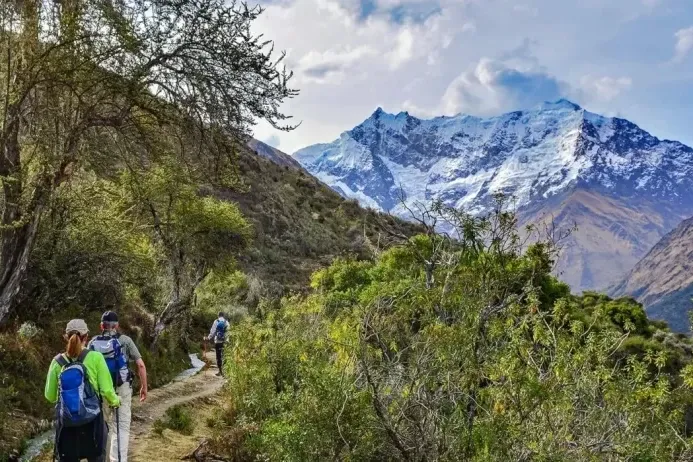 Hikers following a path next to an ancient water channel with a panoramic view of the Humantay and Salkantay mountains.