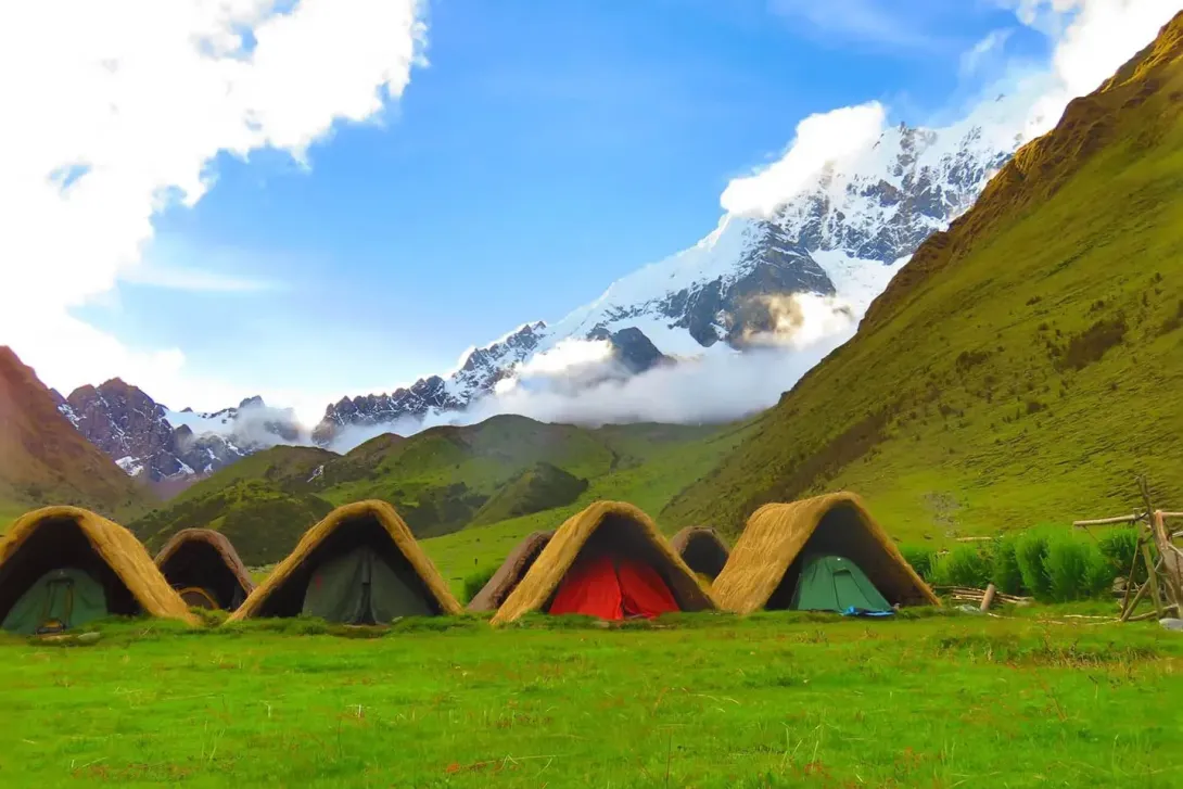 Traditional mountain campsite in the Andes Traditional Andean-style camping huts with thatched roofs in a green valley under the Humantay and Salkantay peaks.