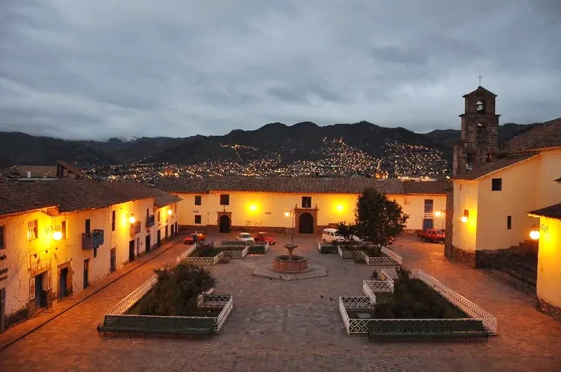 Panoramic view of San Blas plaza and its colonial church at dusk with city lights in the background.