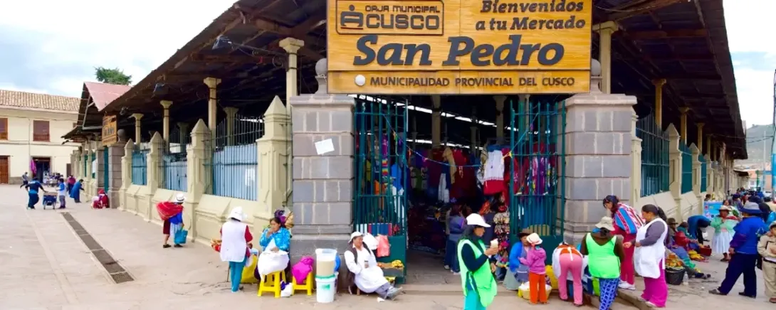 Close-up of the wooden welcome sign at the entrance of San Pedro Market with local people gathering outside.