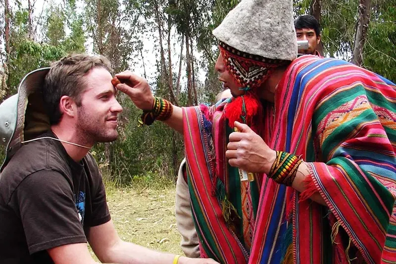 Authentic Shamanic Spiritual Blessing A traditional Andean shaman in colorful attire performing a spiritual cleansing and blessing ritual on a traveler outdoors.