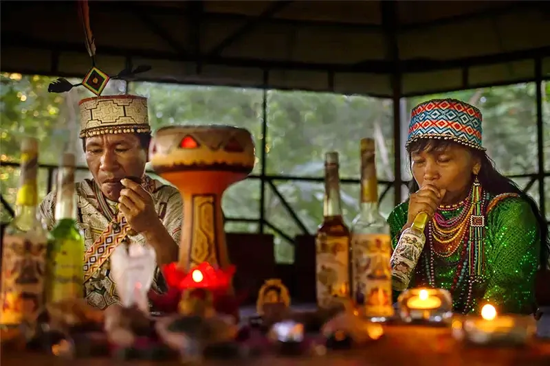 Shipibo Healers Preparing the Sacred Space Two Shipibo shamans in traditional dress preparing sacred elements and blowing tobacco smoke during an Amazonian ritual.