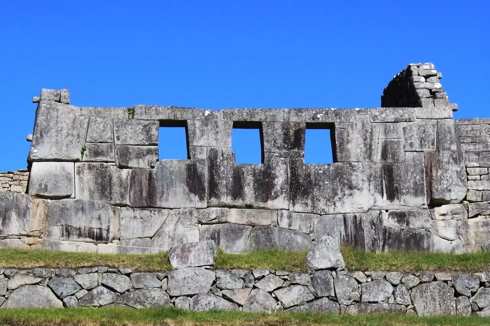 Close-up of the Temple of the Three Windows with perfectly carved Inca stones under a clear blue sky in Machu Picchu.