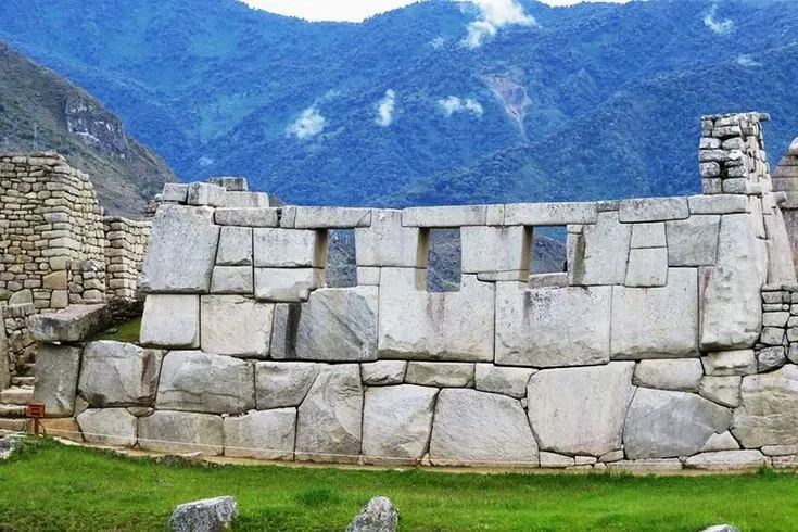 Perspective view of the Temple of the Three Windows with the lush green mountains of the Peruvian Andes in the background.