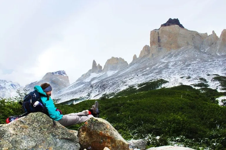 A hiker resting on a rock overlooking the snow-capped granite peaks of Torres del Paine National Park in Patagonia, Chile.