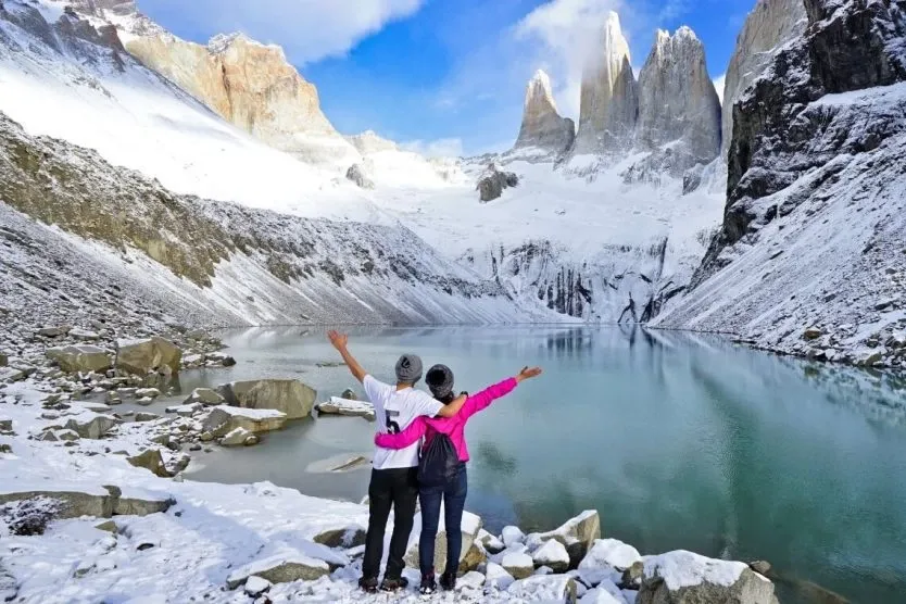 A couple with arms outstretched facing the granite towers and a glacial lake in Torres del Paine, Chile.