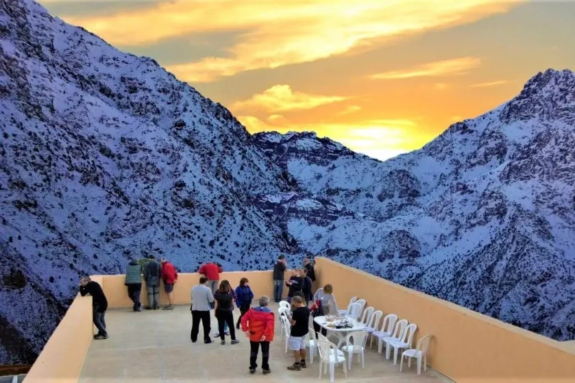 Group of travelers enjoying the sunset on a terrace overlooking the snowy Atlas Mountains in Morocco.