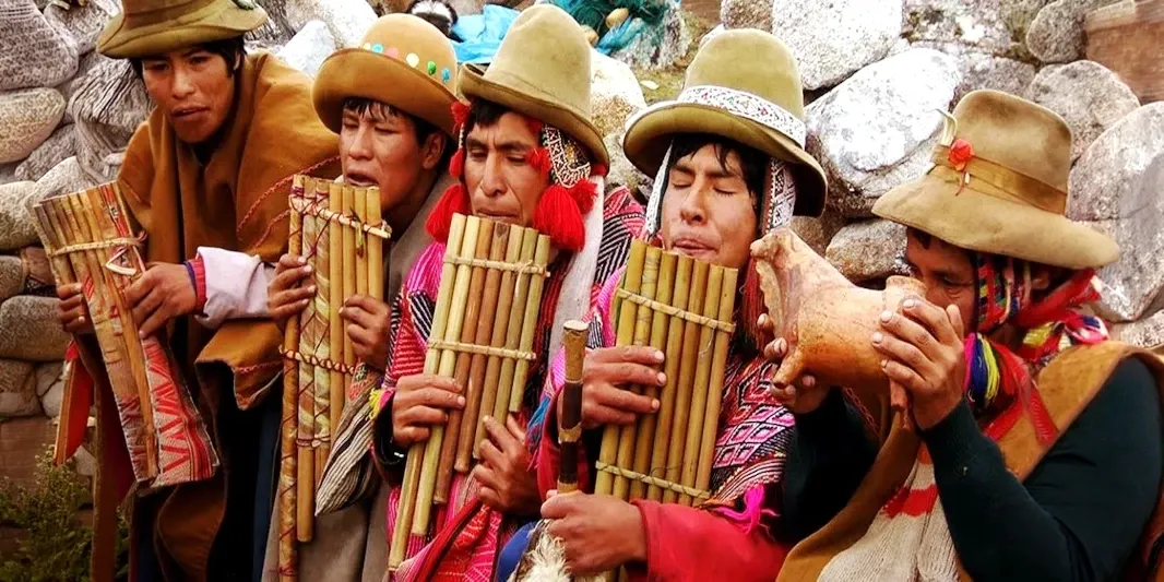 A group of Peruvian men in traditional hats and ponchos playing pan flutes and a shell trumpet during a ceremony.