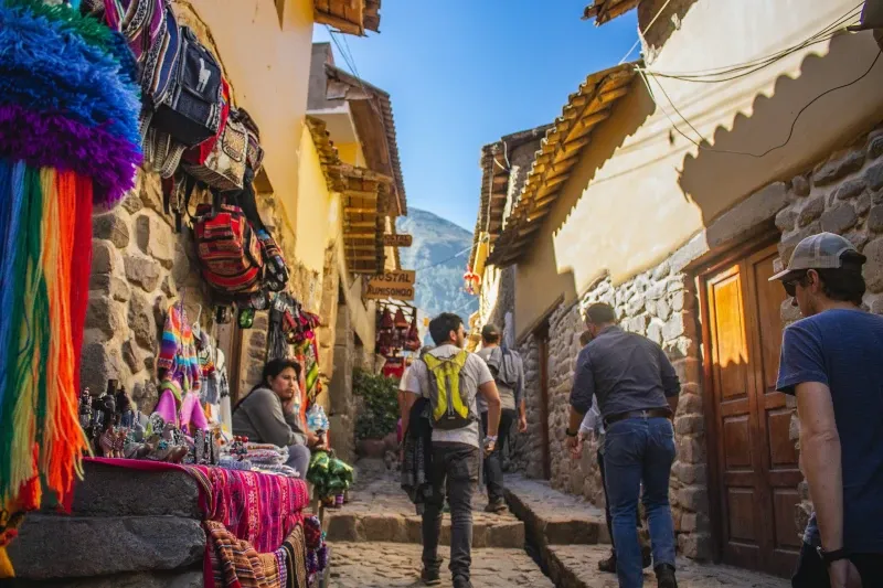 Tourists walking through a narrow cobblestone street in Cusco lined with colorful Peruvian textiles and local handicrafts.