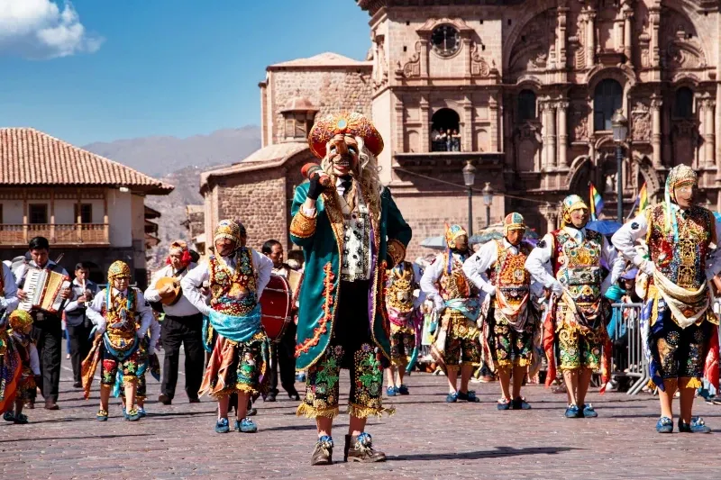 Dancers in colorful traditional costumes performing in front of a colonial church in Cusco.