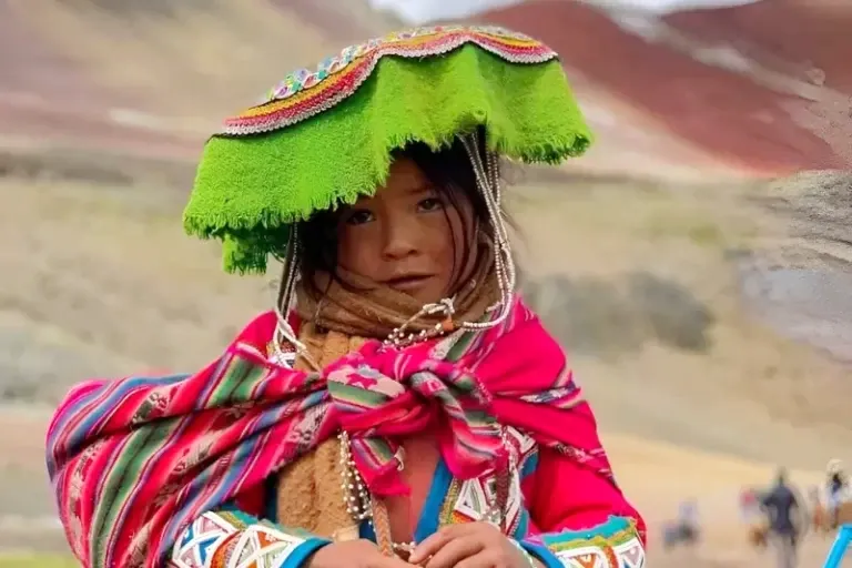Portrait of a young Peruvian girl wearing a traditional green hat and colorful handmade textiles in the mountains.
