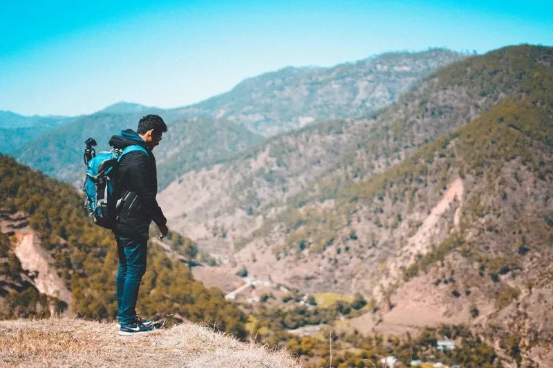 A backpacker standing on a mountain edge looking over a vast green valley during a trek in Peru.
