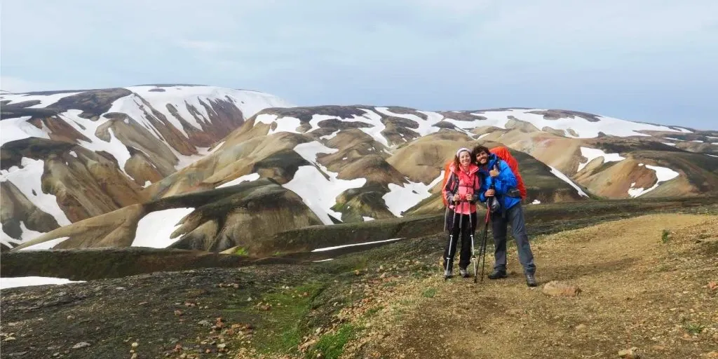 Two hikers with backpacks posing on the Laugavegur trail with snowy mountains in the background.