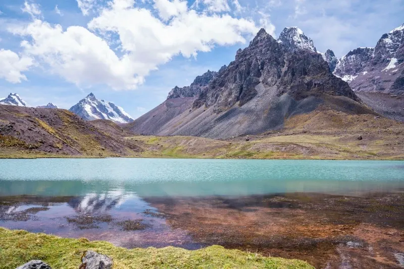 A stunning turquoise mountain lake reflecting the surrounding peaks and clouds during the Ausangate trek.
