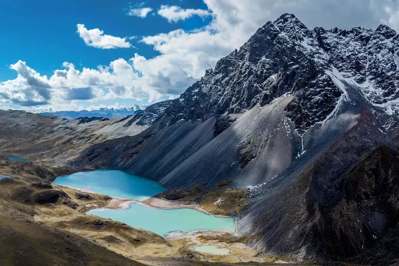High-angle view of two vibrant turquoise glacial lakes at the foot of a rugged, snow-dusted mountain in the Andes.