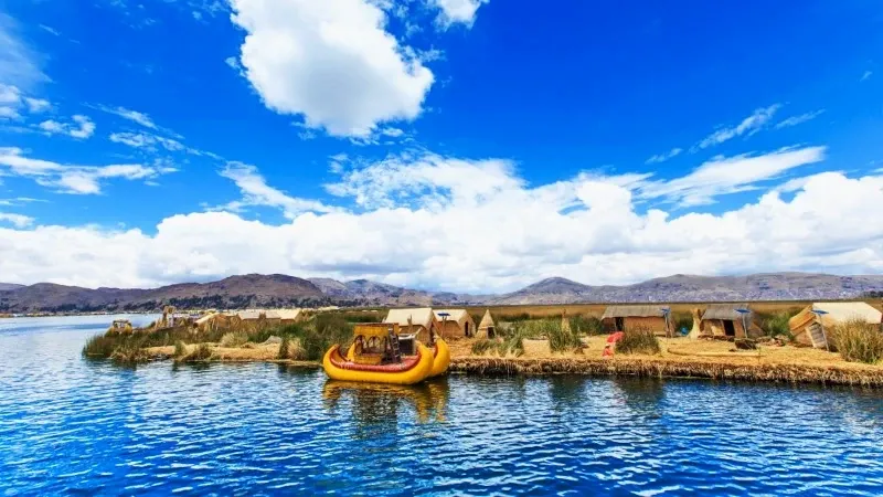 A traditional yellow totora reed boat anchored at a floating island in Lake Titicaca.