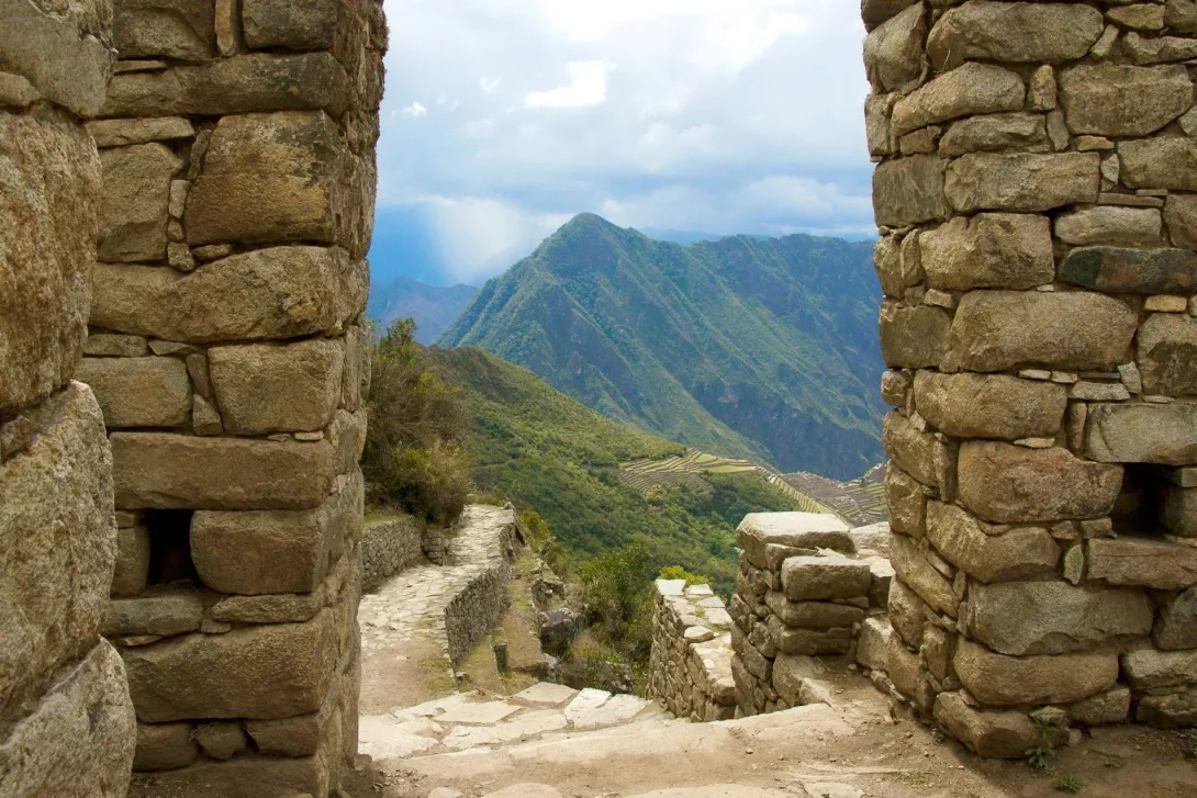 Stone walls of the Sun Gate framing a scenic view of the mountains and the Inca trail leading to Machu Picchu.