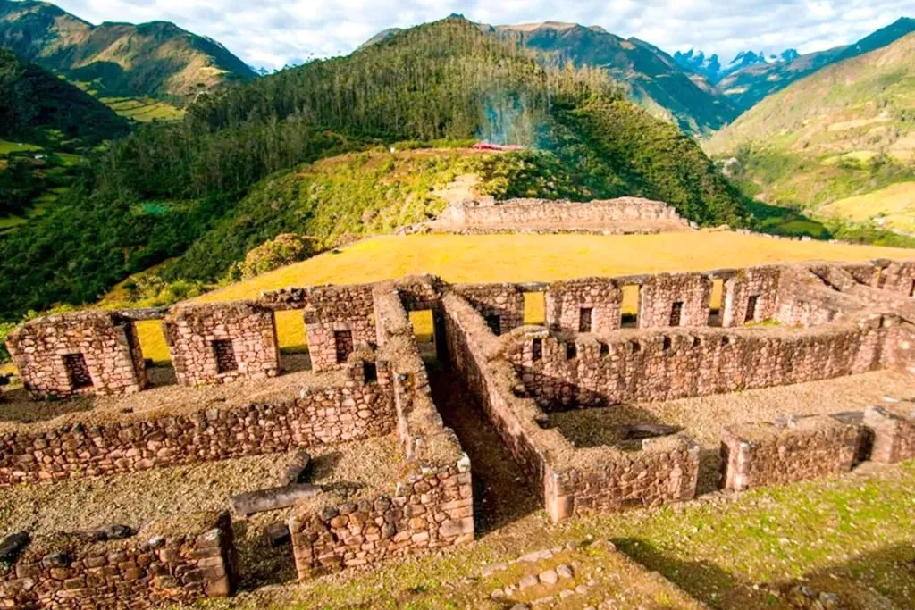 Ancient stone ruins of Vilcabamba with the snow-capped peaks of the Andes in the background under a cloudy sky.