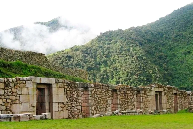 Inca stone walls at the Vilcabamba ruins with clouds descending over the lush cloud forest mountains in Cusco.