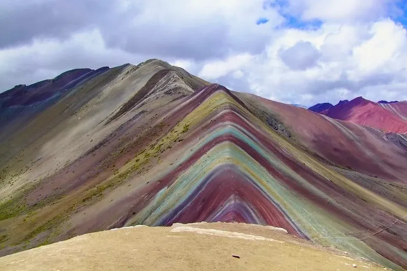 Close-up of the iconic striped peak of the Rainbow Mountain in Peru against a dramatic cloudy sky.