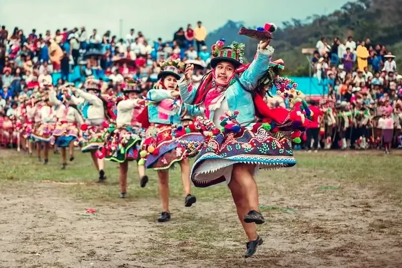 A group of dancers performing the Waynas dance in a large outdoor celebration with a crowd of spectators in the background.