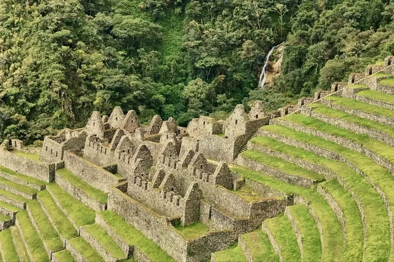 Ancient Inca agricultural terraces and stone ruins at Wiñay Wayna with a waterfall in the distance.