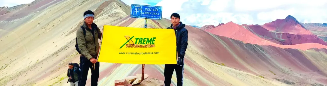 Xtreme Tourbulencia staff members holding the company flag at the summit of Vinicunca Rainbow Mountain in Cusco.